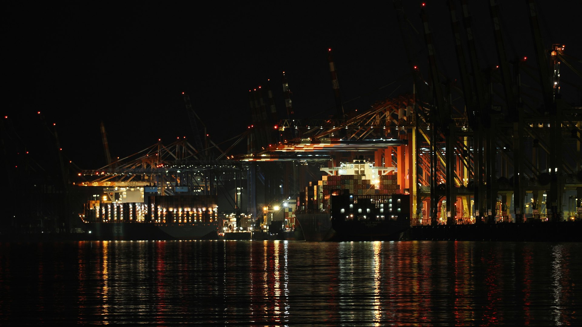 Grúas y buque portacontenedores iluminados en un puerto de noche